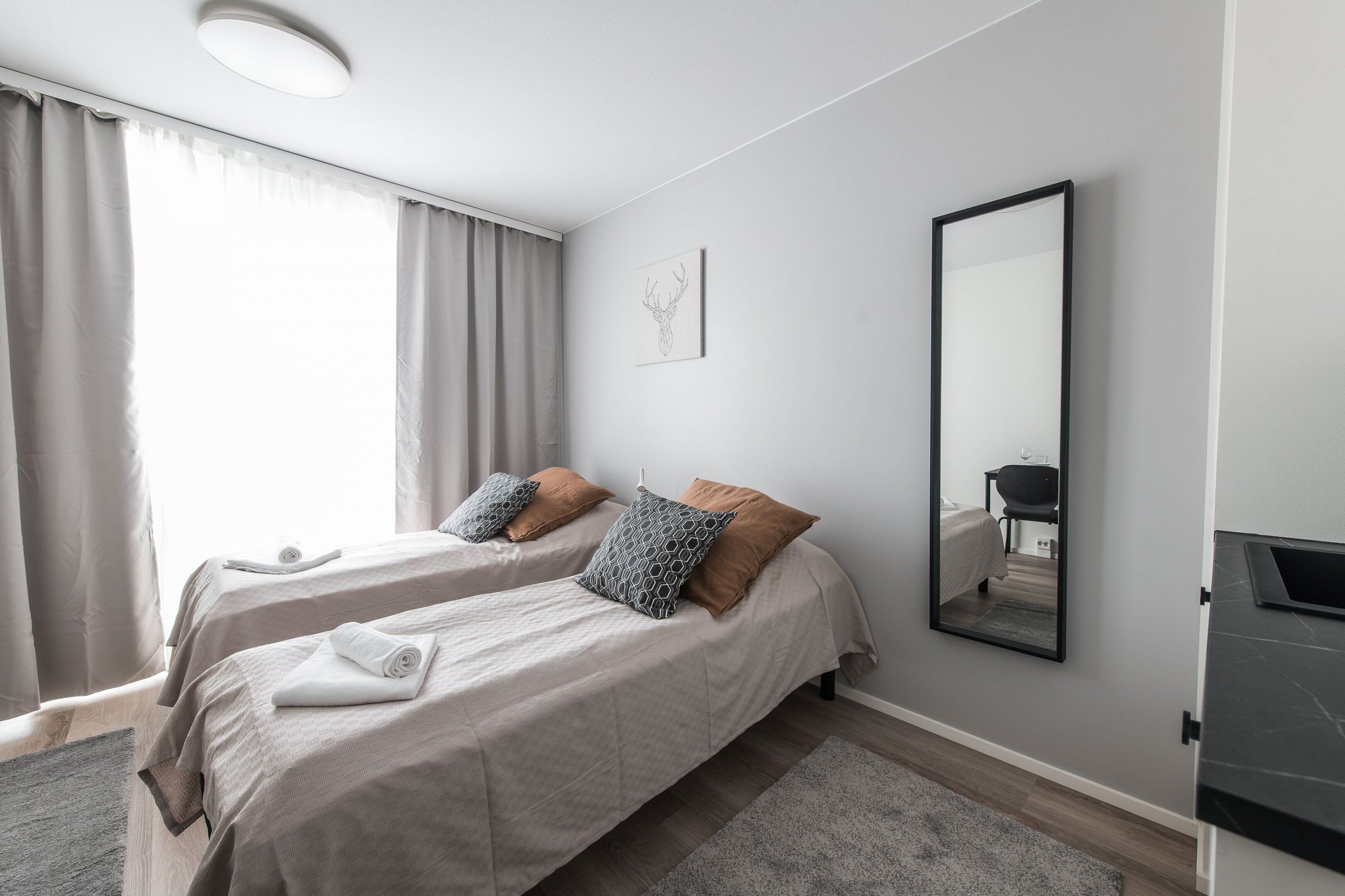 A modern hotel room with two beds, a large mirror, and a desk.