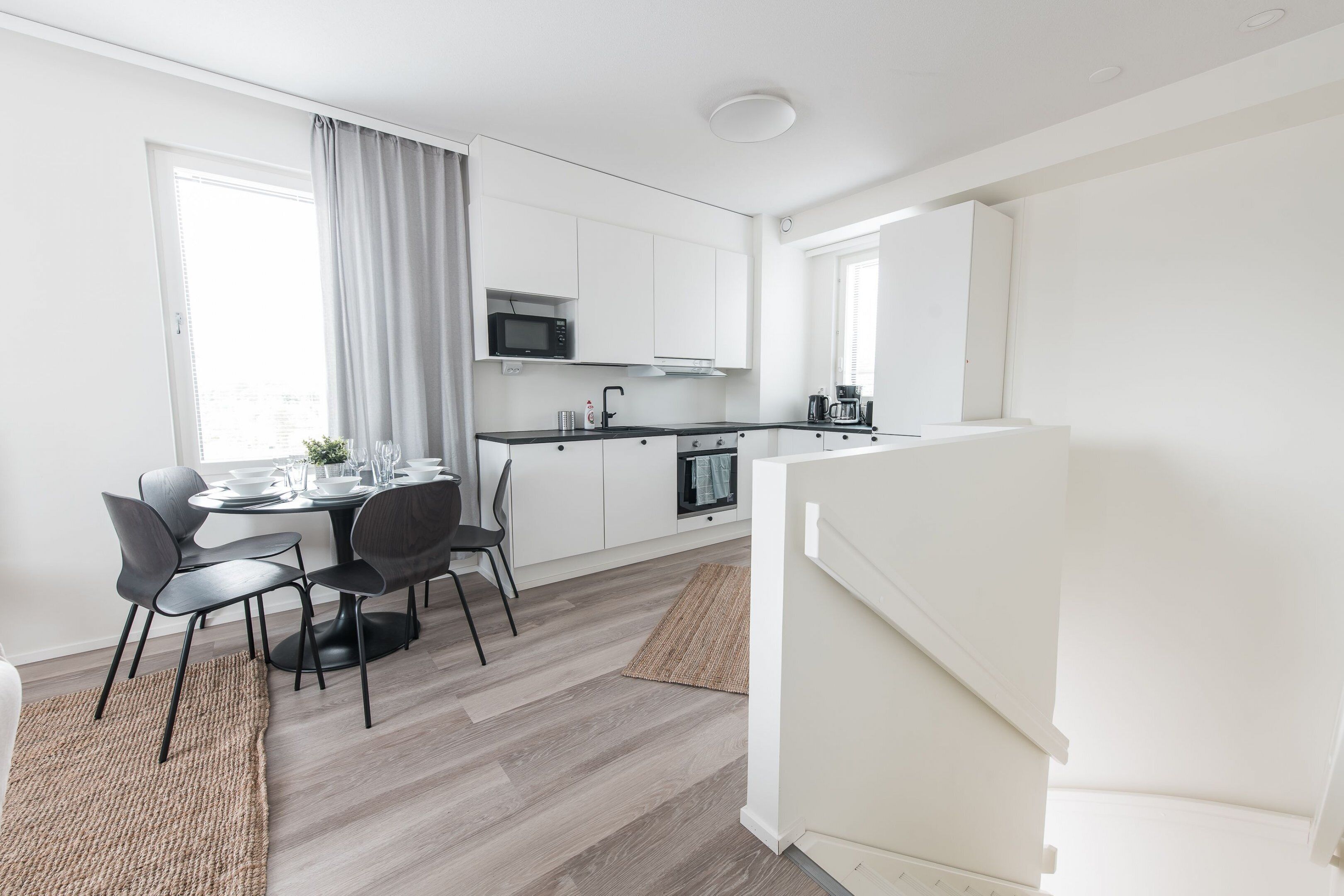 Een moderne keuken met witte kastjes, een magnetron en een eethoek met een tafel en stoelen.