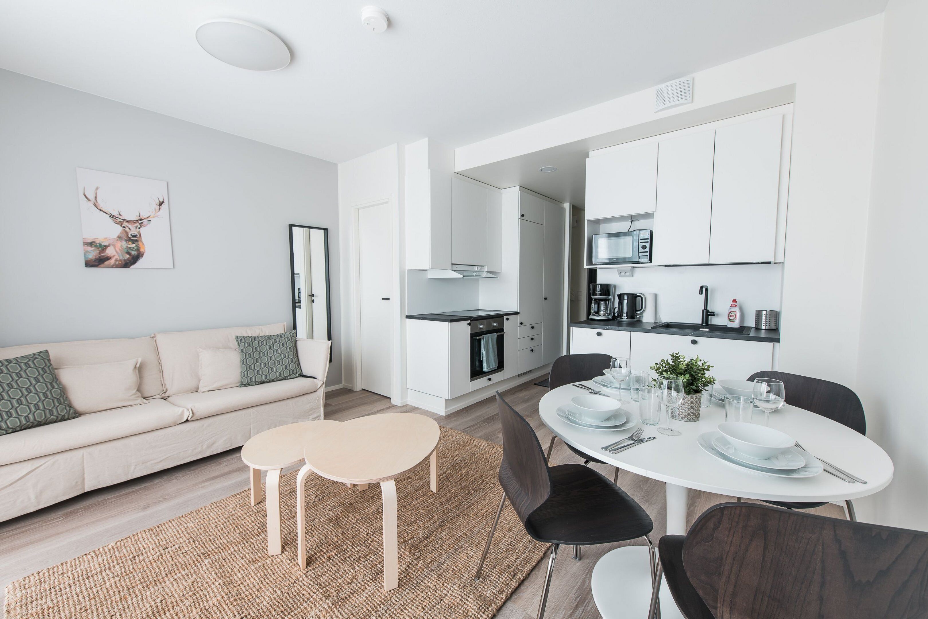Une cuisine moderne avec des meubles blancs, une table à manger pour quatre personnes et un coin salon avec un canapé et une table basse.