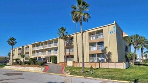 Un hotel de varios pisos con balcones, palmeras y un cielo azul despejado.