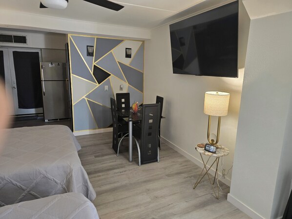 A hotel room with a bed, a desk with a chair, a television mounted on the wall, and a lamp on a small table. - Cozy studio on Padre Island. (Corpus Christi)