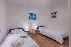 A twin room with two beds, a nightstand with a lamp, a teddy bear, and a magazine on the bed. - Beachside House Lara (Omisalj)