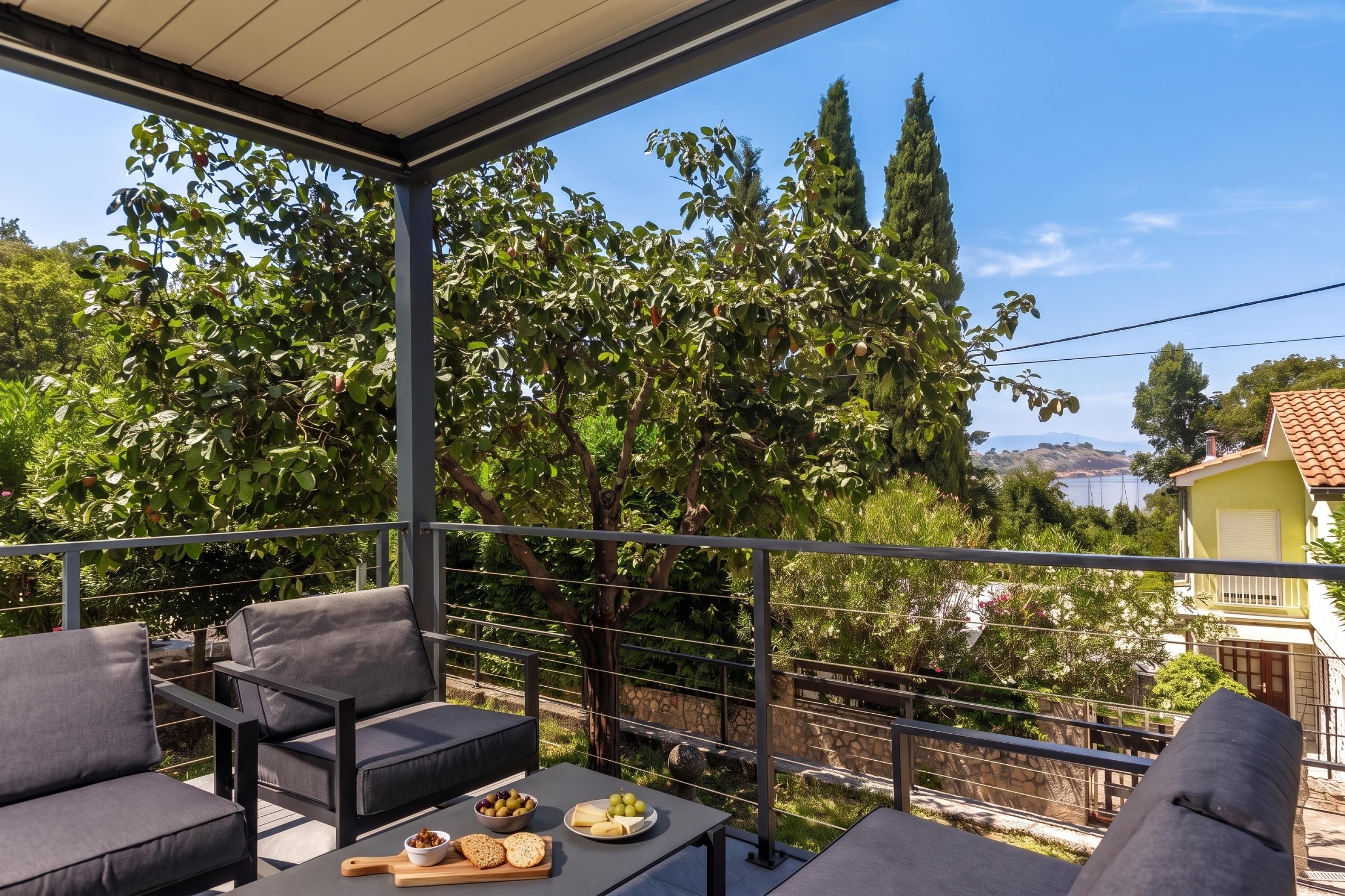 Un balcón con mobiliario exterior y una mesa dispuesta con comida, con vistas a un paisaje de árboles y una lejana vista de agua.