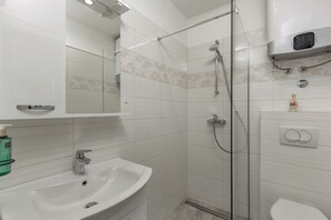 A modern bathroom with a glass-enclosed shower, a white sink, and a toilet. - Beachside House Lara (Omisalj)
