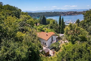 A house with a red roof, surrounded by lush greenery and a lake with boats. - Beachside House Lara (Omisalj)