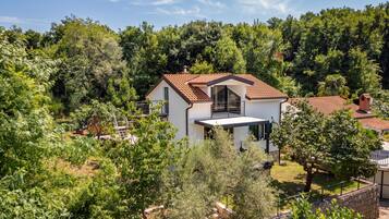 A modern two-story house with a tiled roof, surrounded by dense greenery.