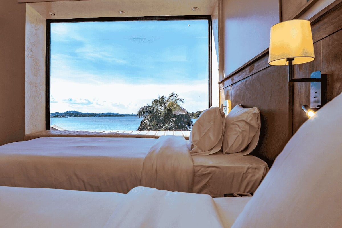 A hotel room with a large window offering a view of the sea and palm trees.