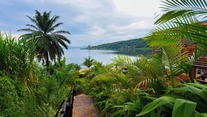 A stone pathway leading to a view of a lake surrounded by lush greenery and palm trees. - Divine Resort & Spa (Kampala)