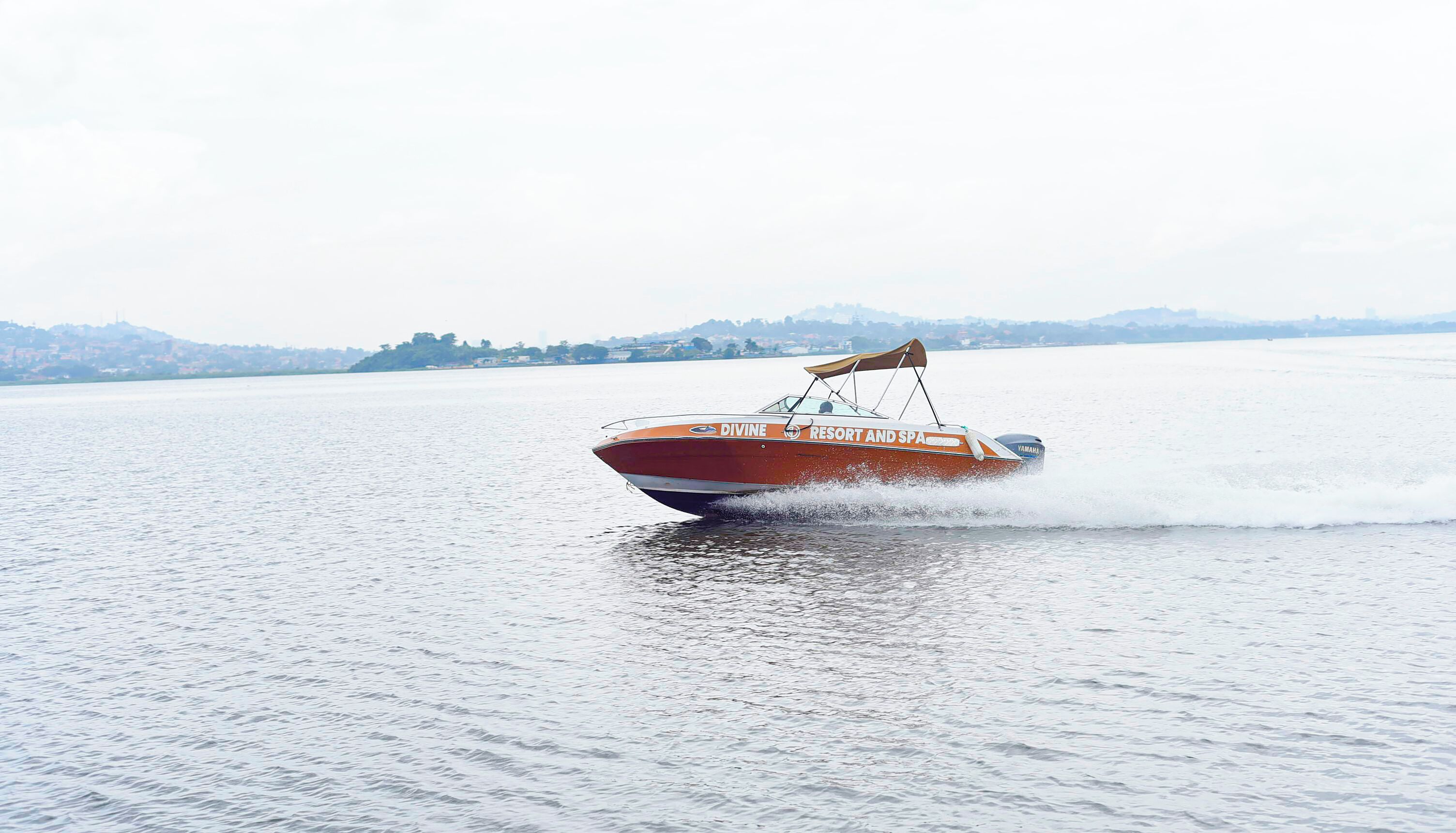 A speedboat with "Divine Resort and Spa" branding on its side, moving across a calm body of water.
