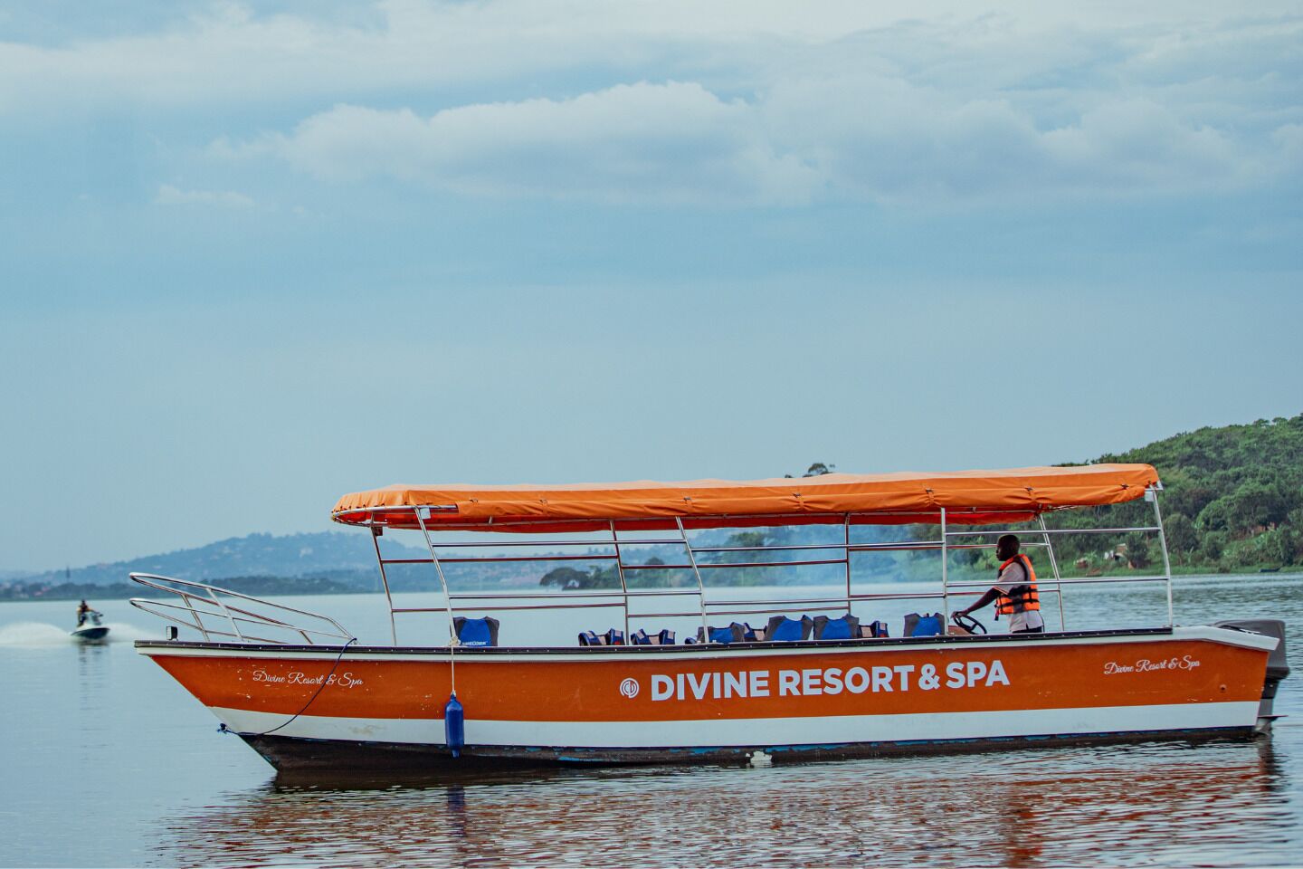 Un bote con toldo naranja y una persona con chaleco salvavidas, identificado como 'DIVINE RESORT & SPA'.