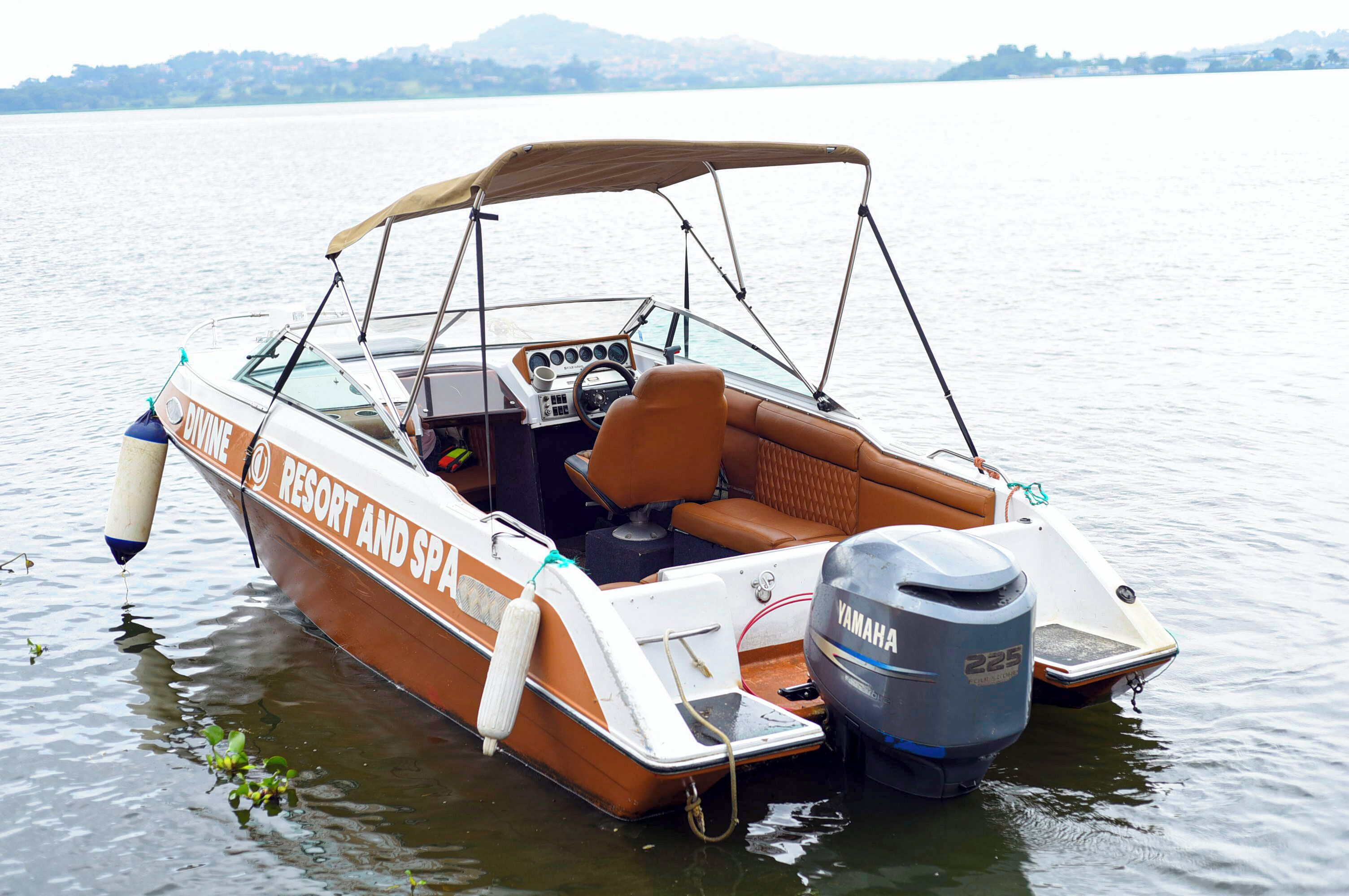 A boat with a canopy, labeled "Divine Resort and Spa," docked on a calm lake.