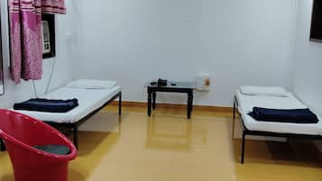 A room with two single beds, a red chair, a small table, and a wall-mounted heater.