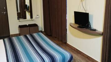A bedroom with a bed, a TV on a shelf, a mirror, and a door.