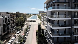 A modern multi-story building with balconies, a central pedestrian walkway, and a parking area. - AVA Hotel & Residences Athens Riviera (Kallithea)