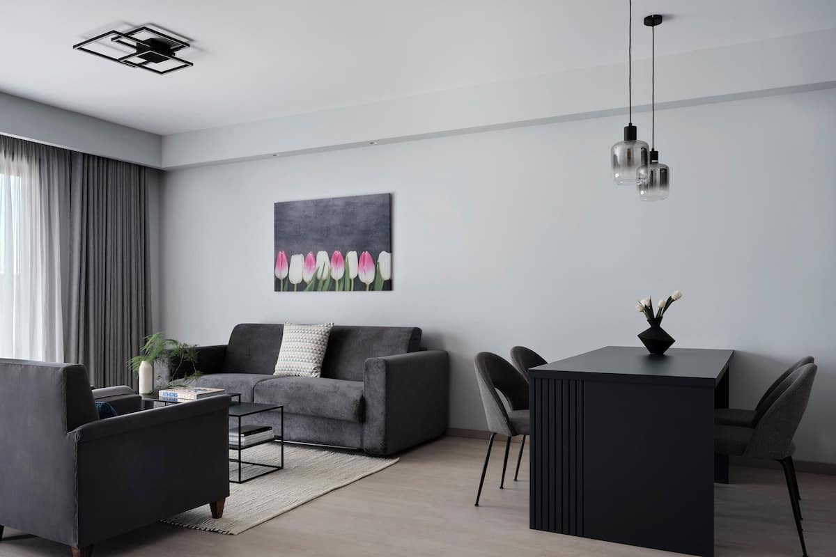 Una sala de estar moderna con un sofá gris, una mesita auxiliar, una mesa de centro y una zona de comedor con una mesa y sillas negras.