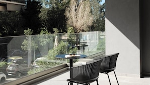 A balcony with a glass railing, two black chairs, and a small round table with a glass and a book. - AVA Hotel & Residences Athens Riviera (Kallithea)