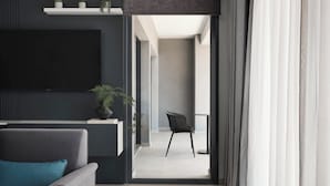 A modern living room with a sofa, a chair, a flat-screen TV, and a potted plant. - AVA Hotel & Residences Athens Riviera (Kallithea)