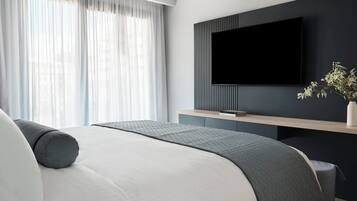 A modern bedroom with a bed, a TV mounted on the wall, and a window with sheer curtains.