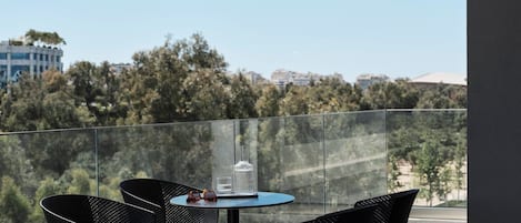 Un balcón con baranda de vidrio, dos sillas negras, una mesita redonda y un par de gafas de sol sobre la mesa.