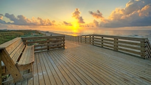 Une promenade en bois menant à une plage, avec un coucher de soleil en arrière-plan.