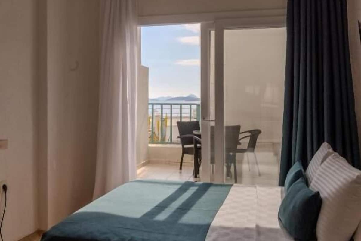 Un dormitorio con cama, vista al balcón y un área de comedor.