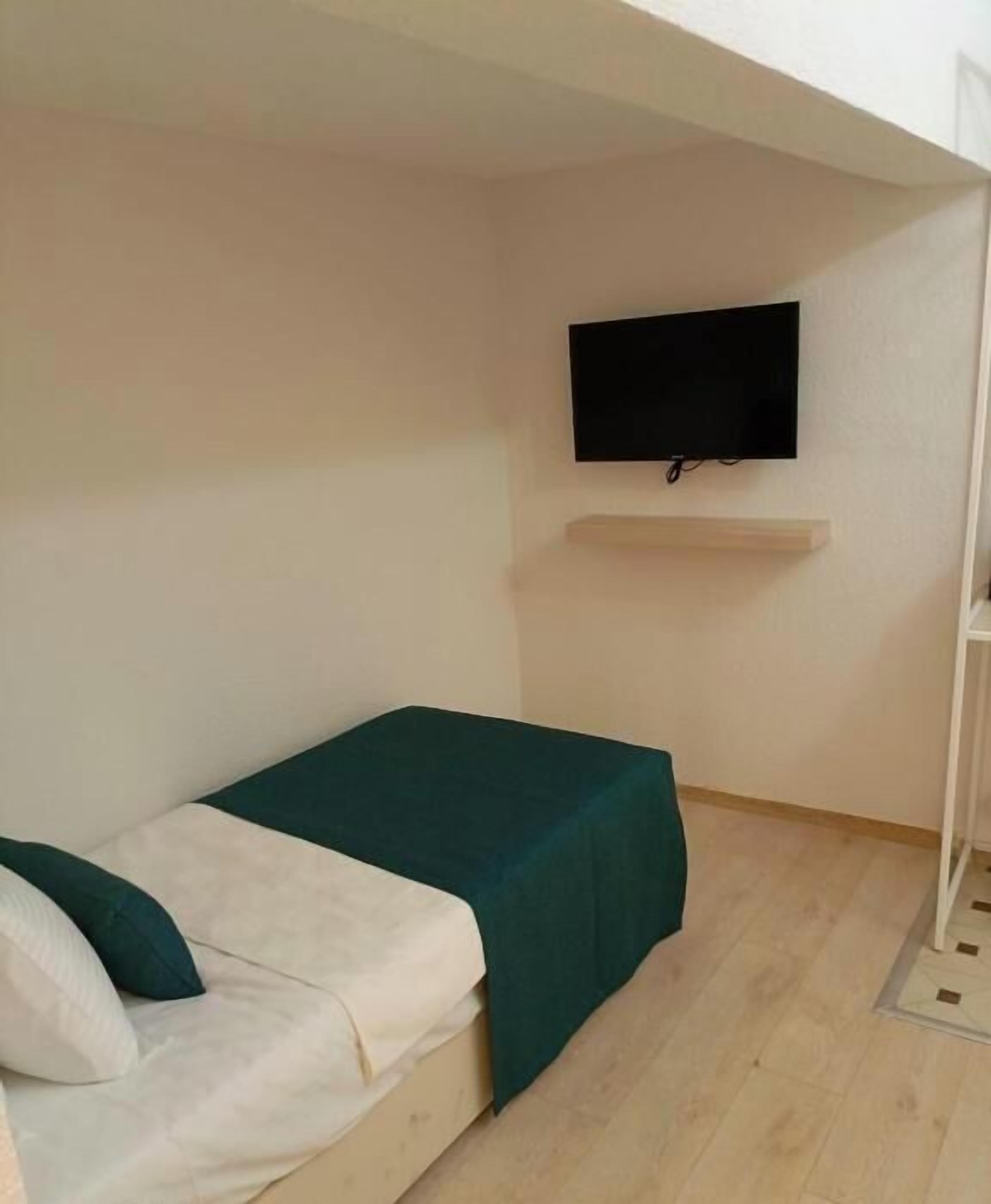 Una habitación pequeña con una cama individual, televisión montada en la pared y suelo de madera.