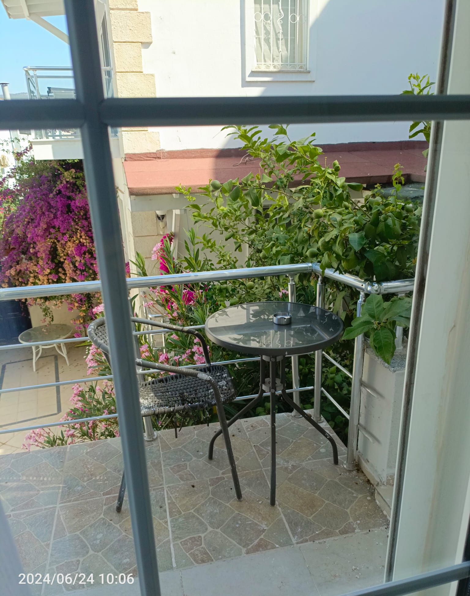 An outdoor patio with a round table and two chairs, surrounded by potted plants and flowers.