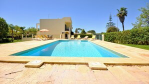 A rectangular swimming pool with a clear blue water, surrounded by a light-colored tiled deck. There are lounge chairs and umbrellas along the poolside. - Villa in Vilamoura near Falésia Beach (Quarteira)