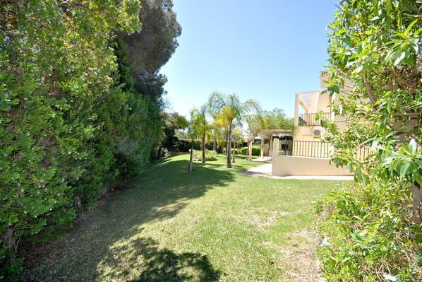 A well-maintained garden with a pathway leading to a building with a balcony. - Villa in Vilamoura near Falésia Beach (Quarteira)