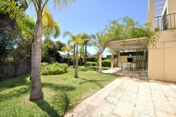 A courtyard with a pergola, palm trees, and a seating area with tables and chairs. - Villa in Vilamoura near Falésia Beach (Quarteira)