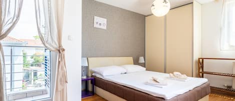 A hotel room with a bed, a bedside table, a lamp, a wardrobe, and a window with curtains.