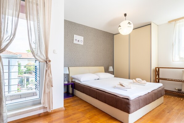 A hotel room with a bed, a nightstand, a lamp, a wardrobe, and a window with curtains.