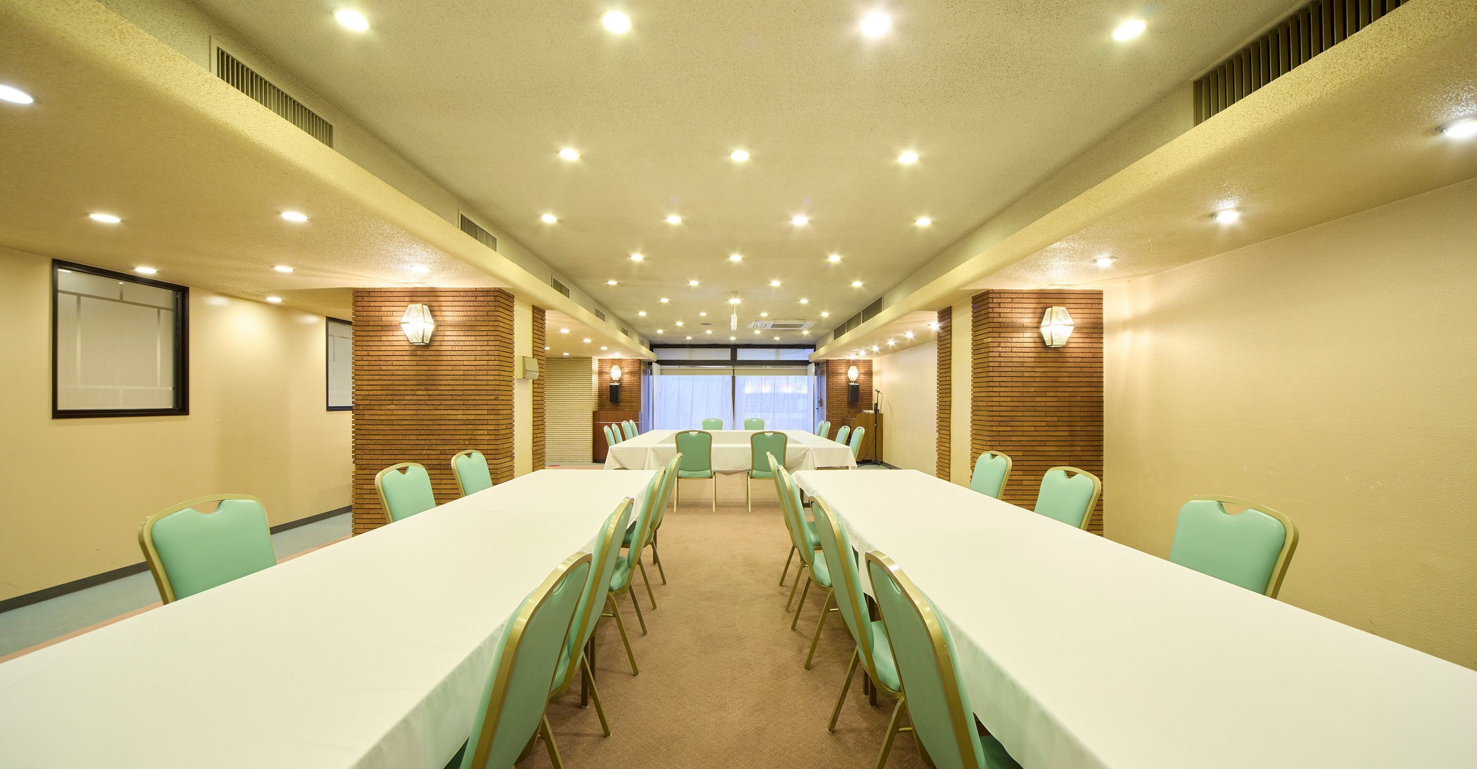 Una sala de conferències amb taules llargues i cadires, una pantalla de projector i vistes cap a l'exterior.