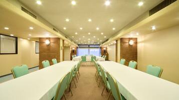 Un salón de conferencias con mesas y sillas largas, una pantalla de proyector y vistas al exterior.
