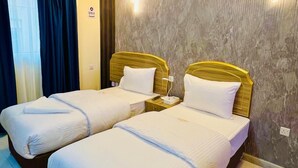 A hotel room with two beds, a nightstand, a wall-mounted light, and a window with curtains. - GALAXY STAR HOTEL L.L.C (Dubai)