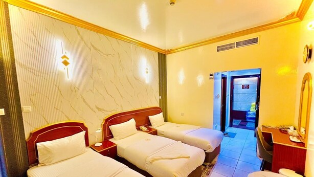 A hotel room with three single beds, a desk with a chair, a small table, and a mirror. - GALAXY STAR HOTEL L.L.C (Dubai)