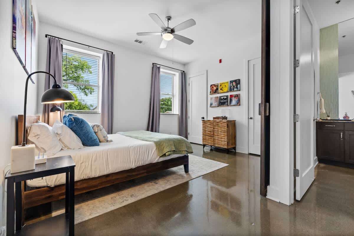 A bedroom with a bed, a ceiling fan, a nightstand, a lamp, a dresser, and a window with curtains.