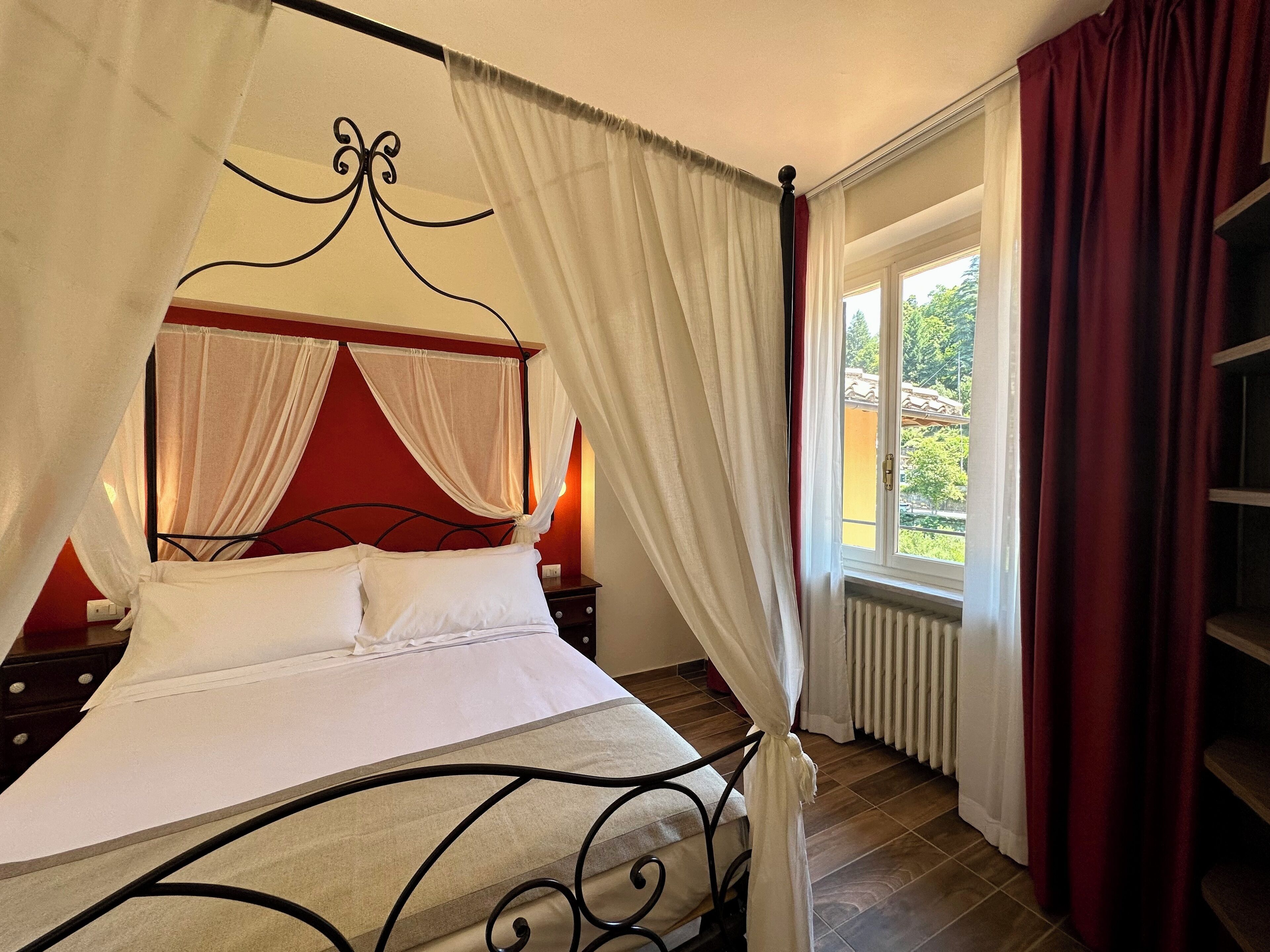A four-poster bed with white linens, a red headboard, and a canopy.