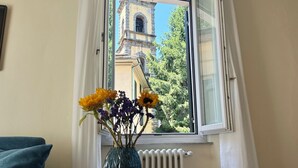 Ein Zimmer mit Fensterblick auf eine Kirche, eine blaue Vase mit Blumen auf einem kleinen Tisch und ein blaues Sofa.