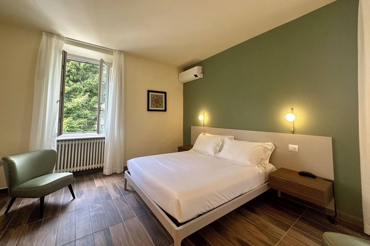 A hotel room with a bed, a chair, a nightstand, and a window with curtains.