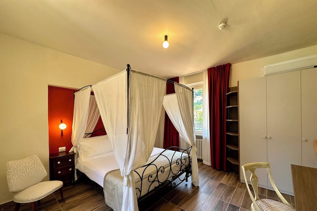 A bedroom with a four-poster bed, a nightstand, a chair, a wardrobe, and a radiator.