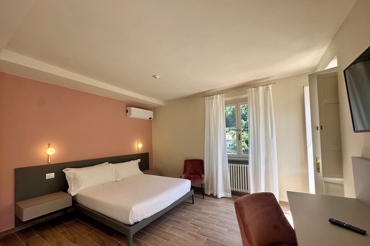 A hotel room with a bed, bedside tables, a chair, a desk, and a TV.