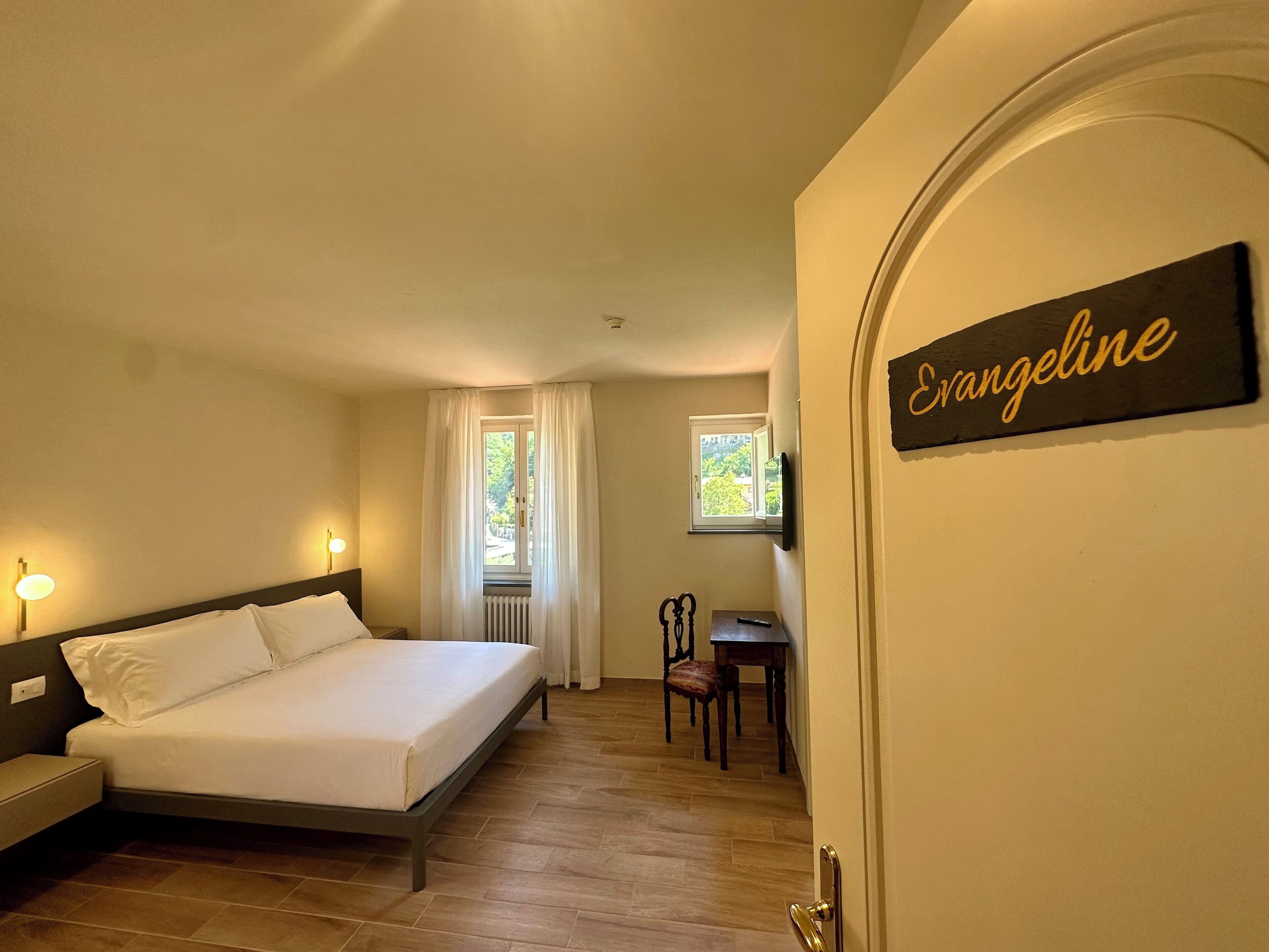 Un dormitorio con cama, mesita de noche, silla, ventana con cortinas, radiador y un cartel en la pared.