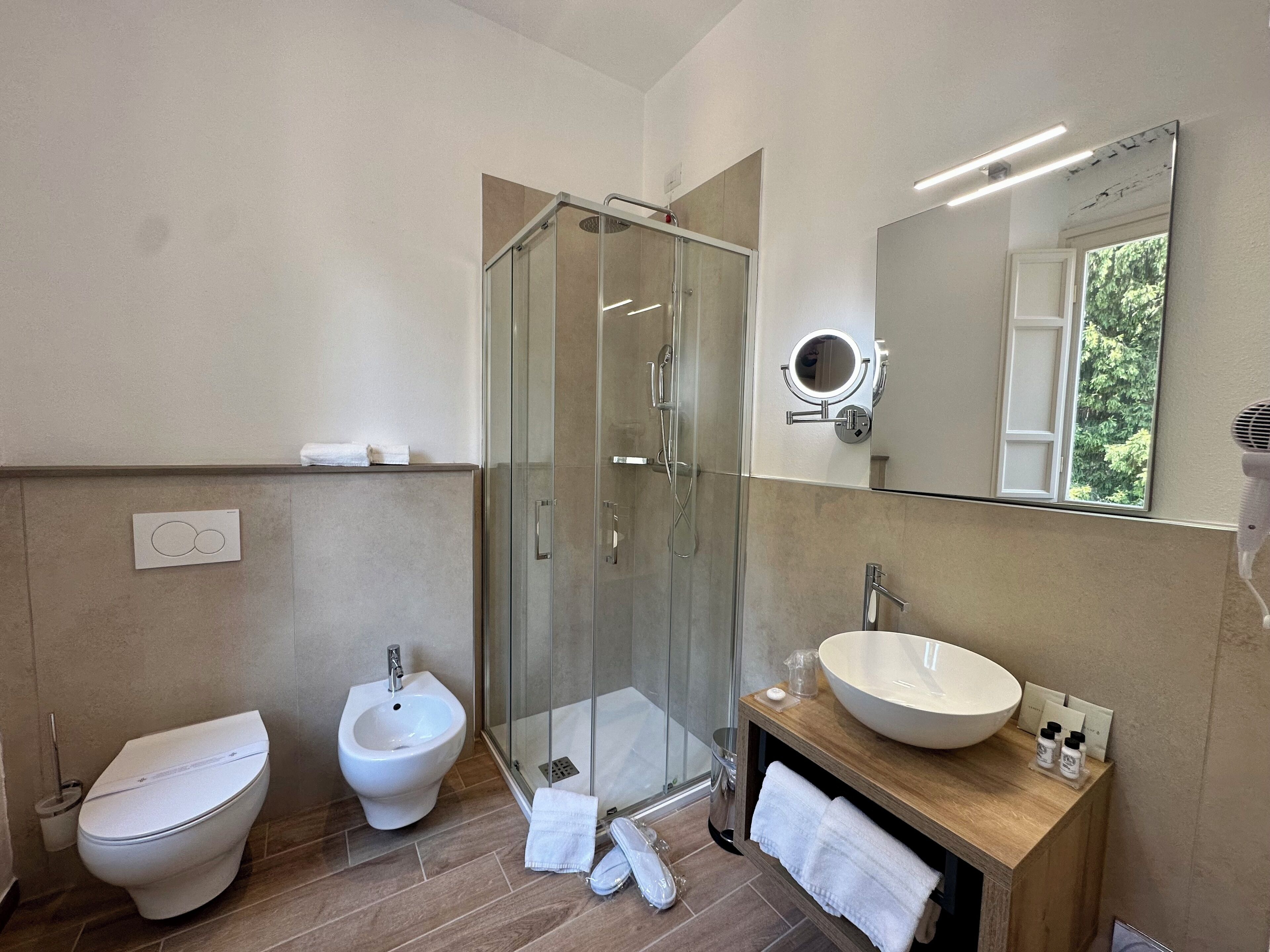 Ein modernes Badezimmer mit einer Duschkabine aus Glas, einem Bidet, einem Waschbecken mit großem Becken und einem Spiegel mit rundem Spiegel darüber.