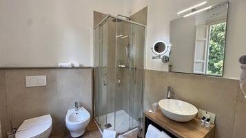 Ein modernes Badezimmer mit einer Duschkabine aus Glas, einem Bidet, einem Waschbecken mit großem Becken und einem Spiegel mit rundem Spiegel darüber.
