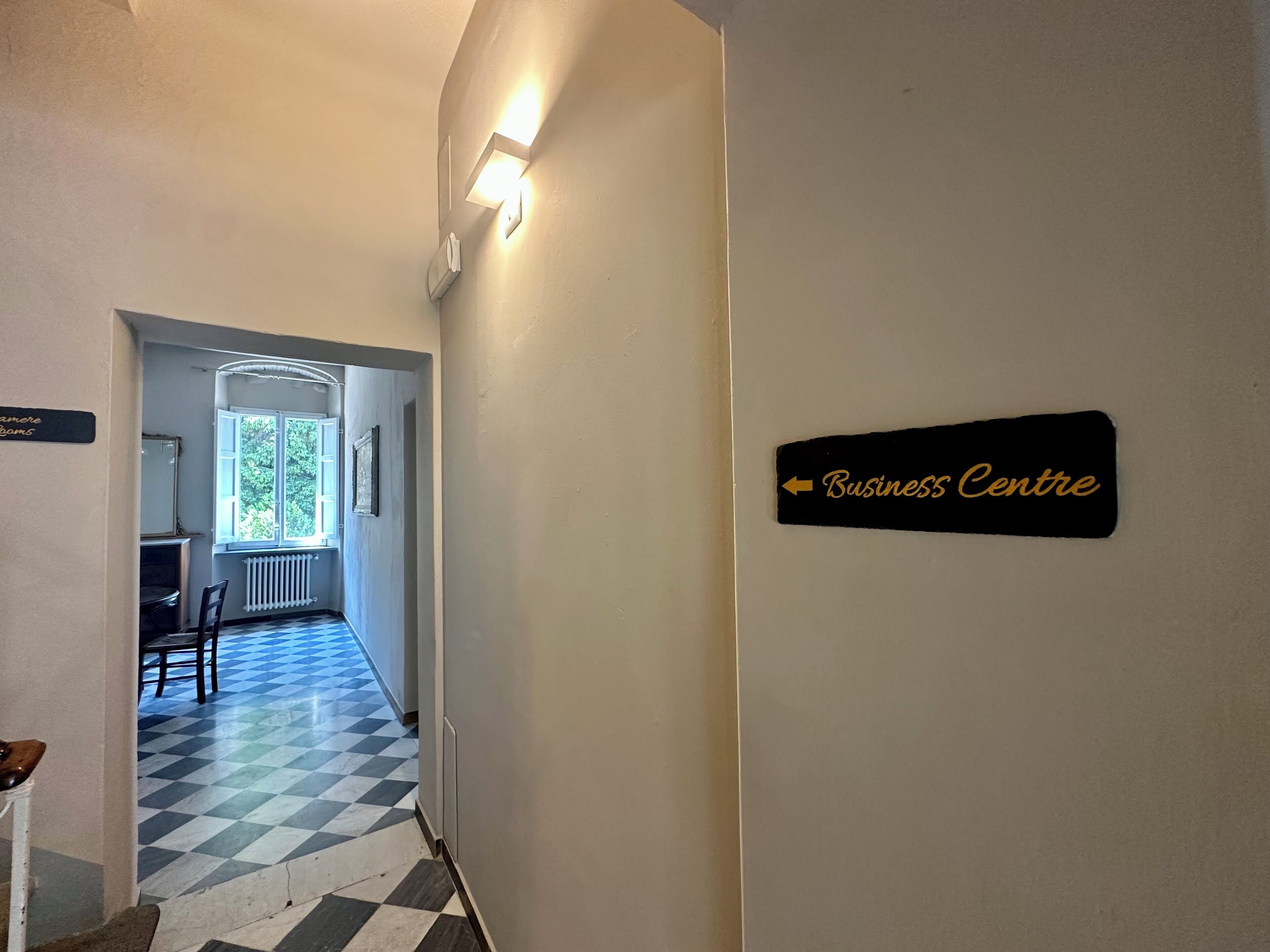 A hallway with a checkered floor, a sign indicating the Business Centre, and a radiator on the wall.