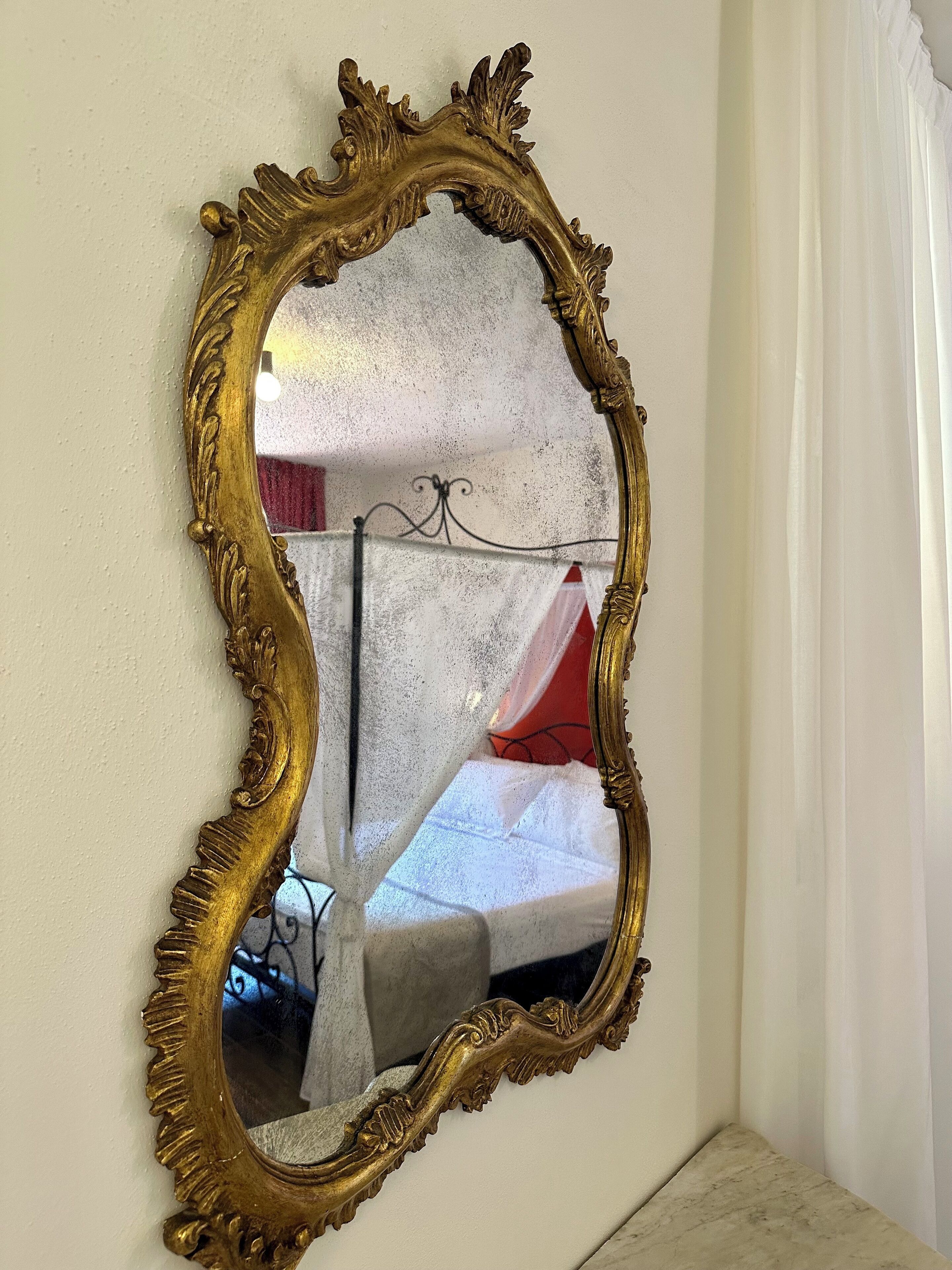 A gold-framed mirror with a decorative design on a wall.
