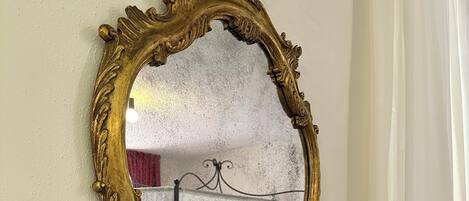 Een spiegel met gouden lijst en decoratieve versiering aan een muur.
