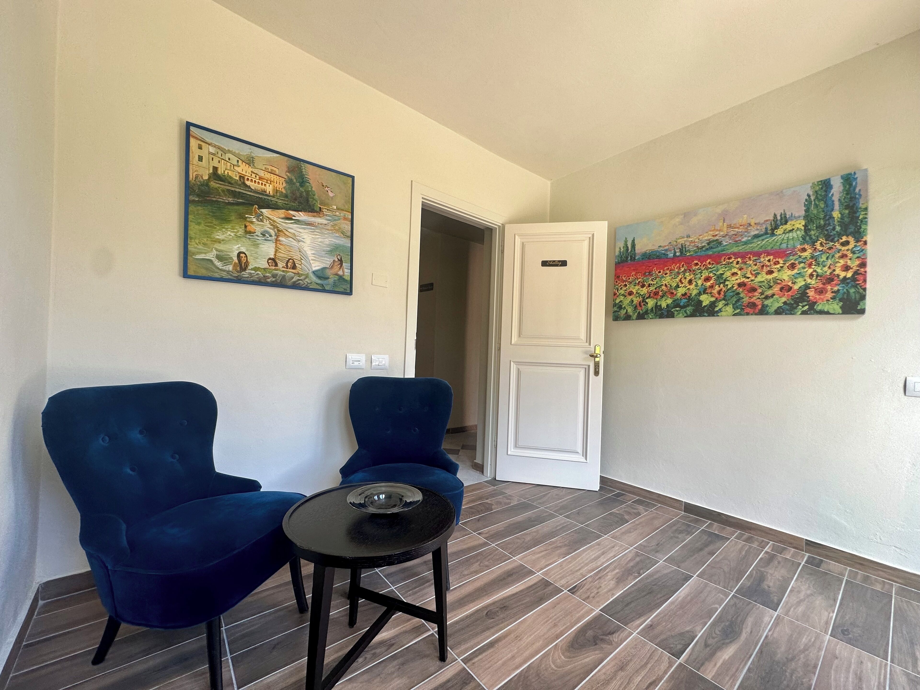 Una habitación con dos sillones azules, una mesita negra y dos cuadros en las paredes.