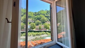 Ein Zimmer mit großem Fenster und Blick auf einen Fluss, Gebäude und Grünflächen.